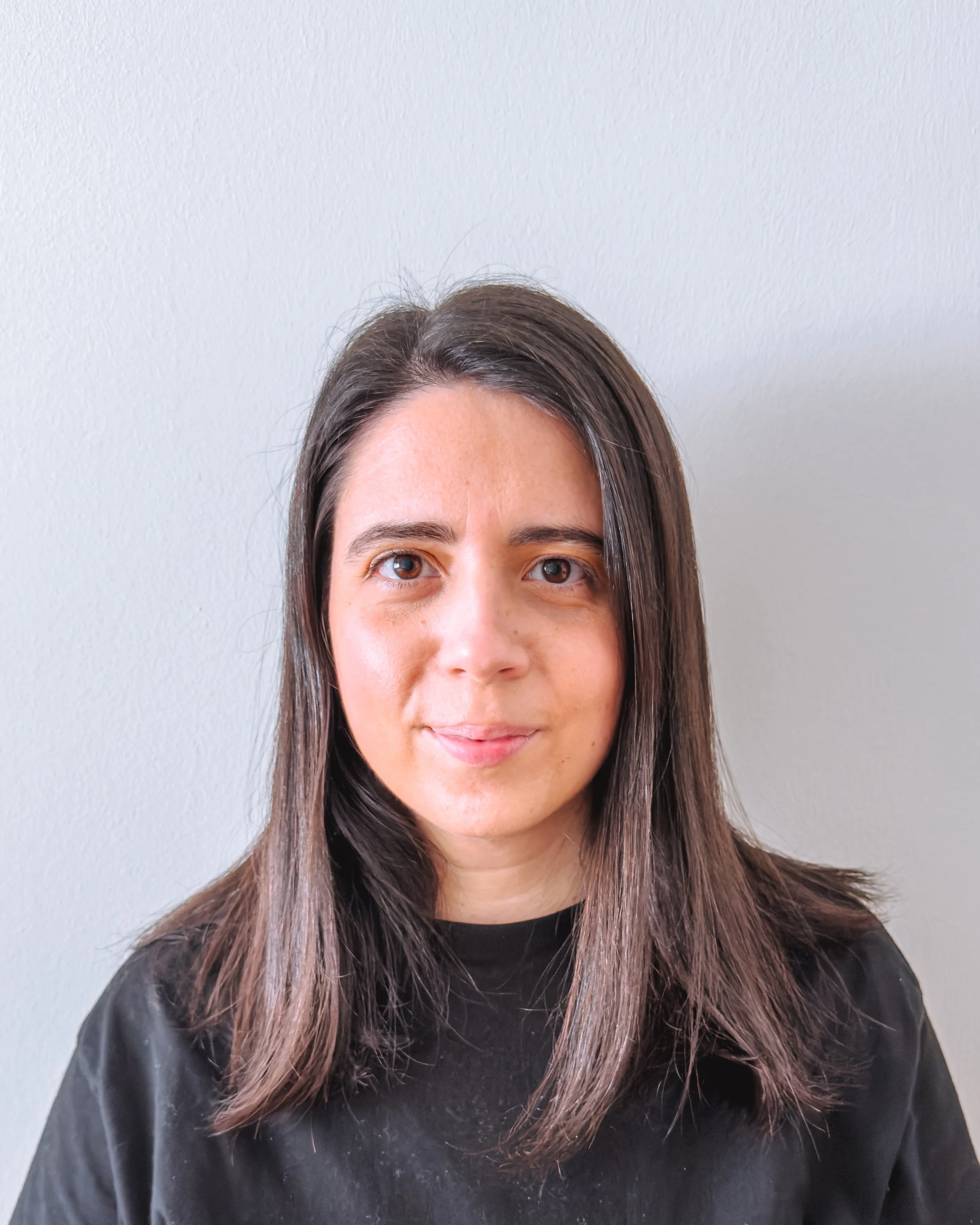 Retrato de uma mulher com cabelos castanhos, olhos castanhos claros, usando blusa preta, contra fundo branco.