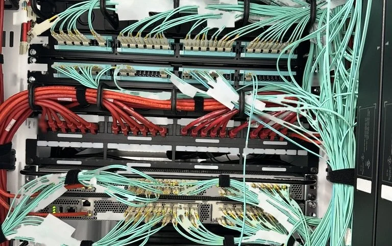 Aqua multimode fiber patch panels above a Cat6 patch panel and switch in a dressed data center rack