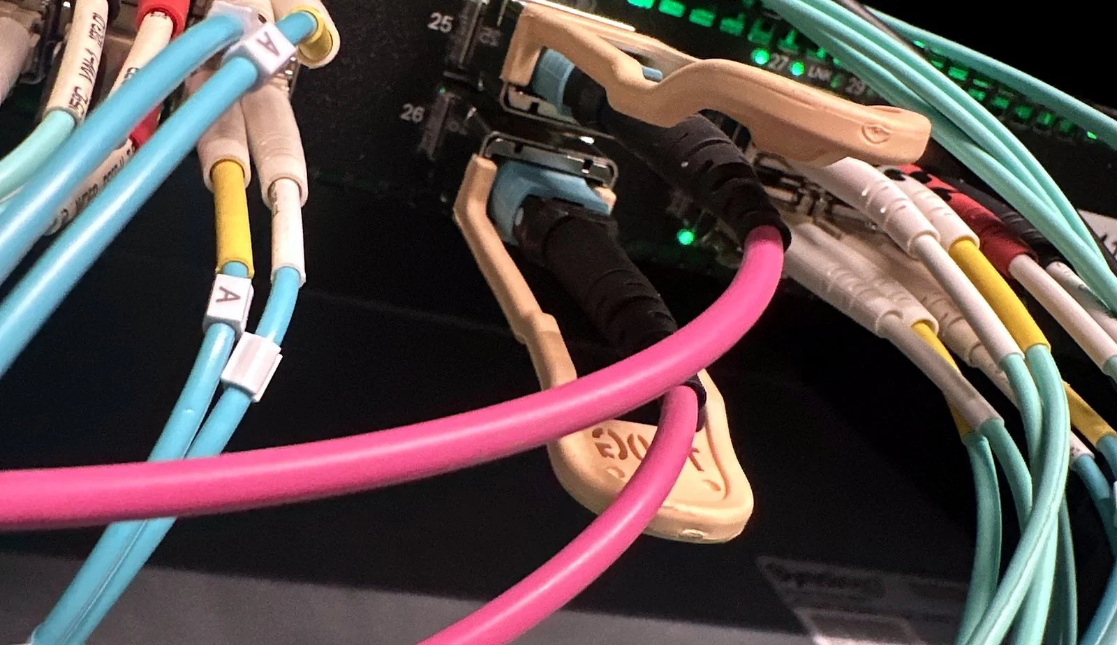 Aqua and pink fiber jumpers patched in a network rack