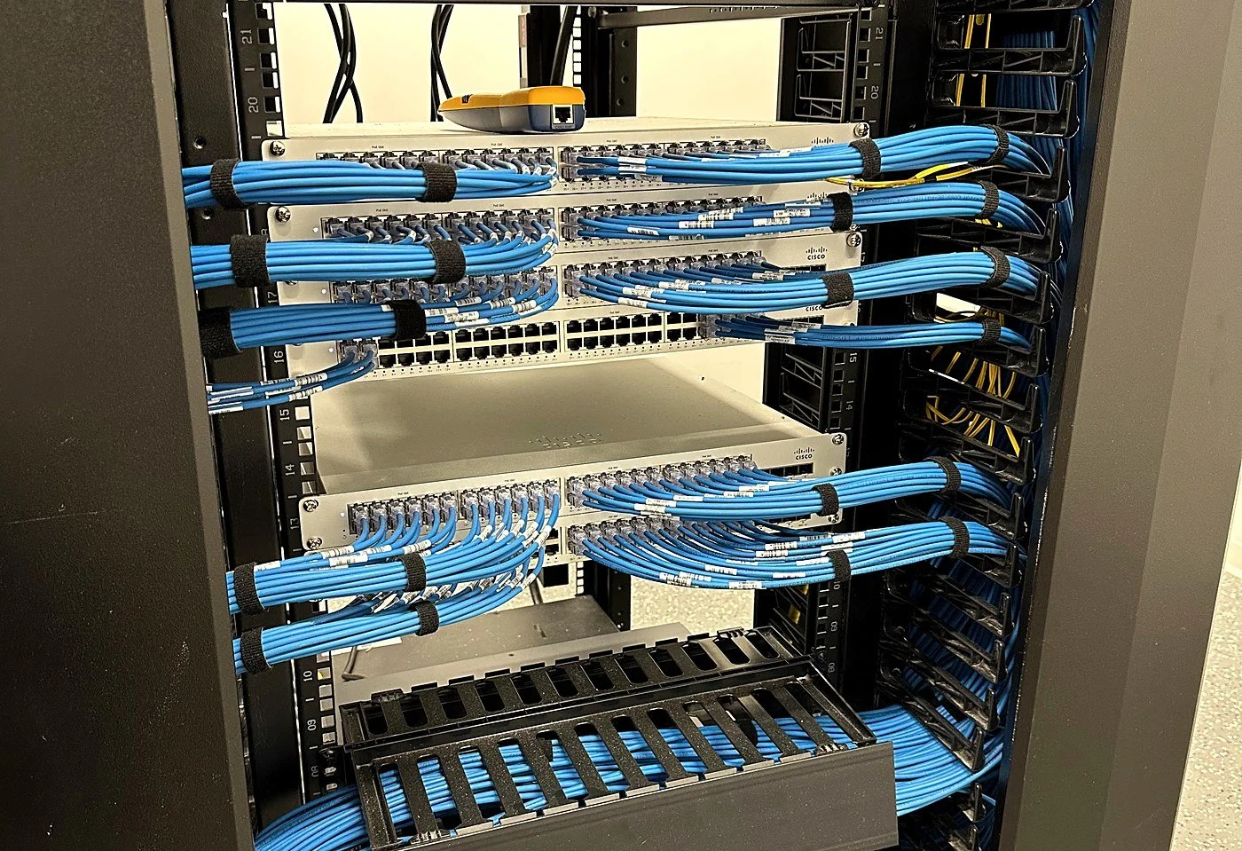 Blue Cat6 patching bundled with hook-and-loop ties into Cisco switches in a network rack