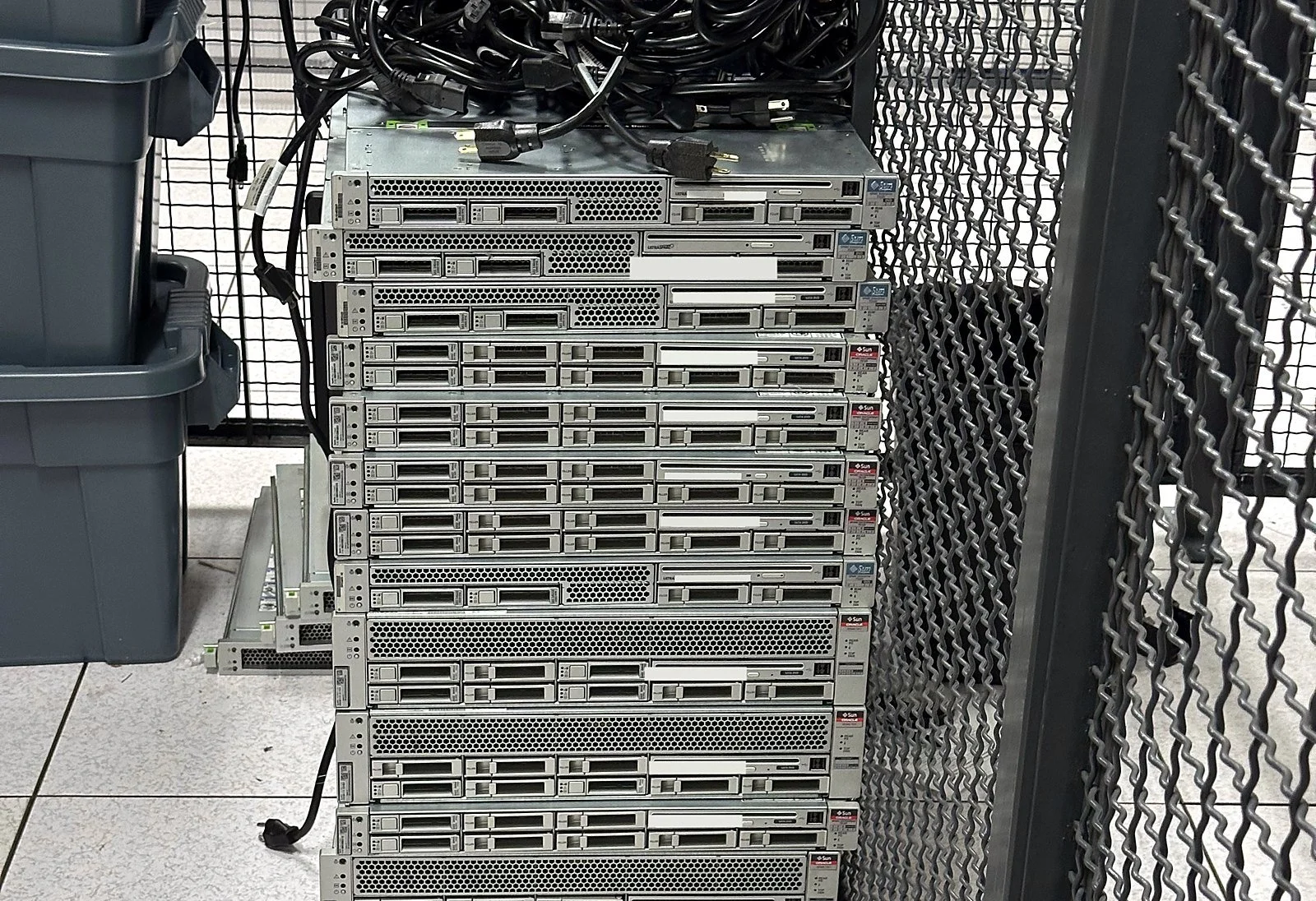 Stack of decommissioned 1U servers with their power cords coiled on top, staged inside a colocation cage