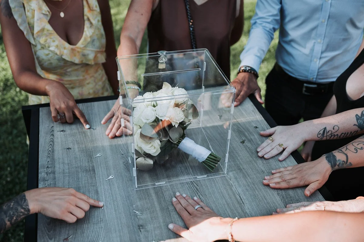 Alternative originale au lancé de bouquet traditionnel : les invitées autour d’un coffret transparent fermé à clé, seule l’une d’elles peut l’ouvrir. Idée d’animation mariage ludique capturée par un photographe professionnel à Paris.