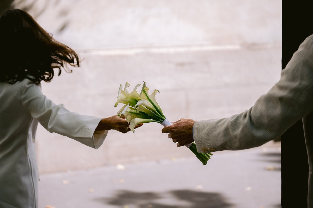 Geste de tendresse : échange d'une fleur entre les deux époux. Photographe de mariage capturant les détails intimes.