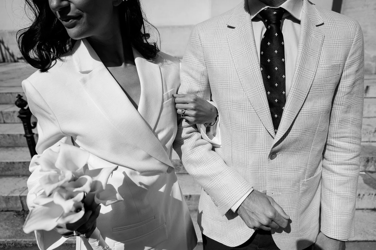 Détail élégant en noir et blanc : enlacement des mariés mettant en valeur le bouquet de fleurs et l'alliance au doigt. Photographie esthétique mariage Paris.