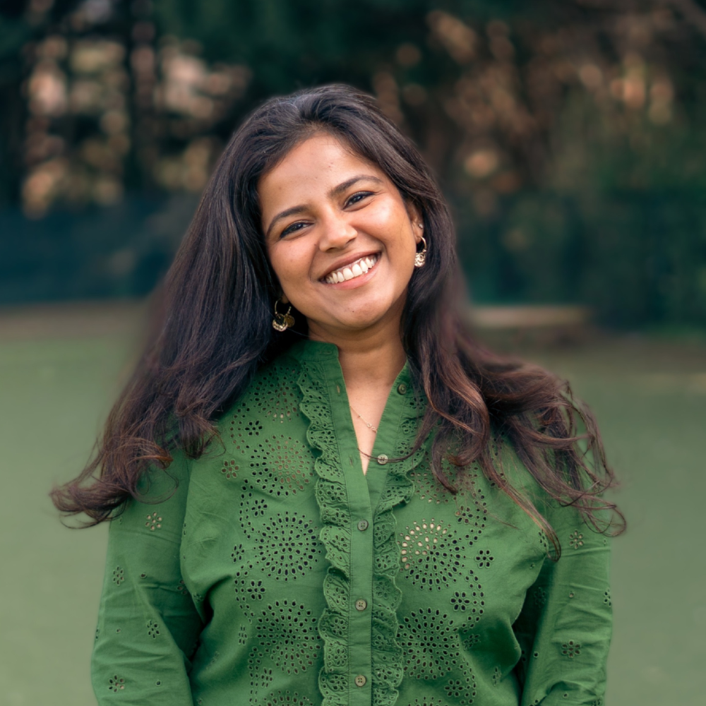 A woman smiling in front of a black backdrop, wearing a patterned high-neck dress and earrings.