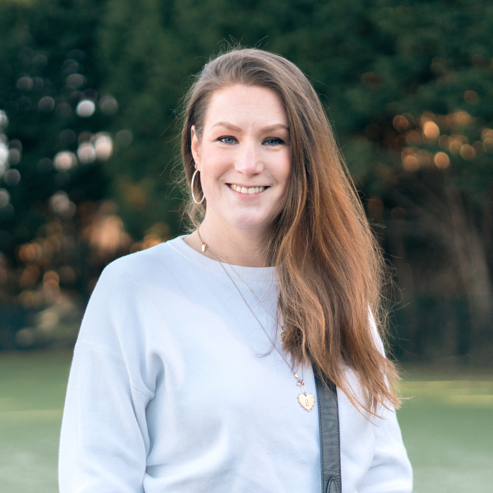 A smiling woman with long brown hair wearing a striped shirt and a smiling man with a beard wearing a brown leather jacket, standing in front of a black background.