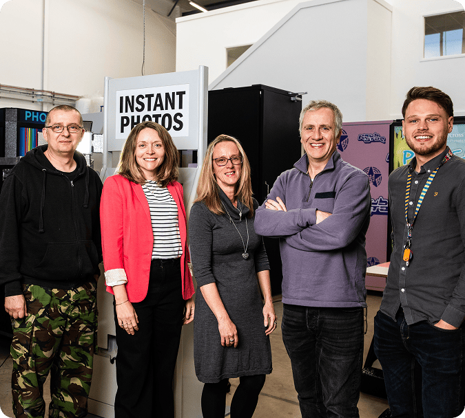 Five colleagues standing in front of an INSTANT PHOTOS booth at a 2026 Games Fleadh event on a college campus