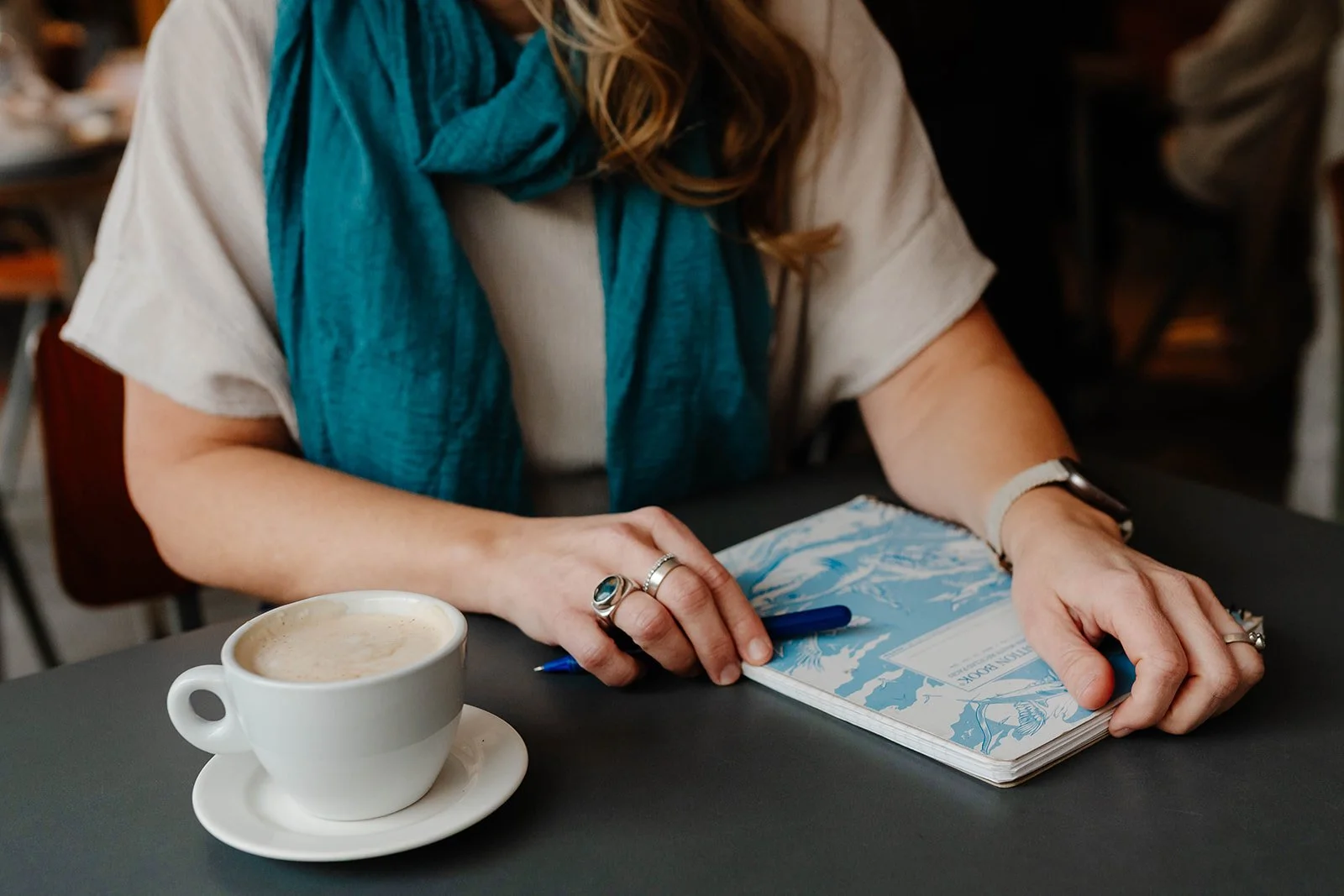 Scenic view of a mountain lake with rolling hills and tall mountains in the background, under a cloudy sky.