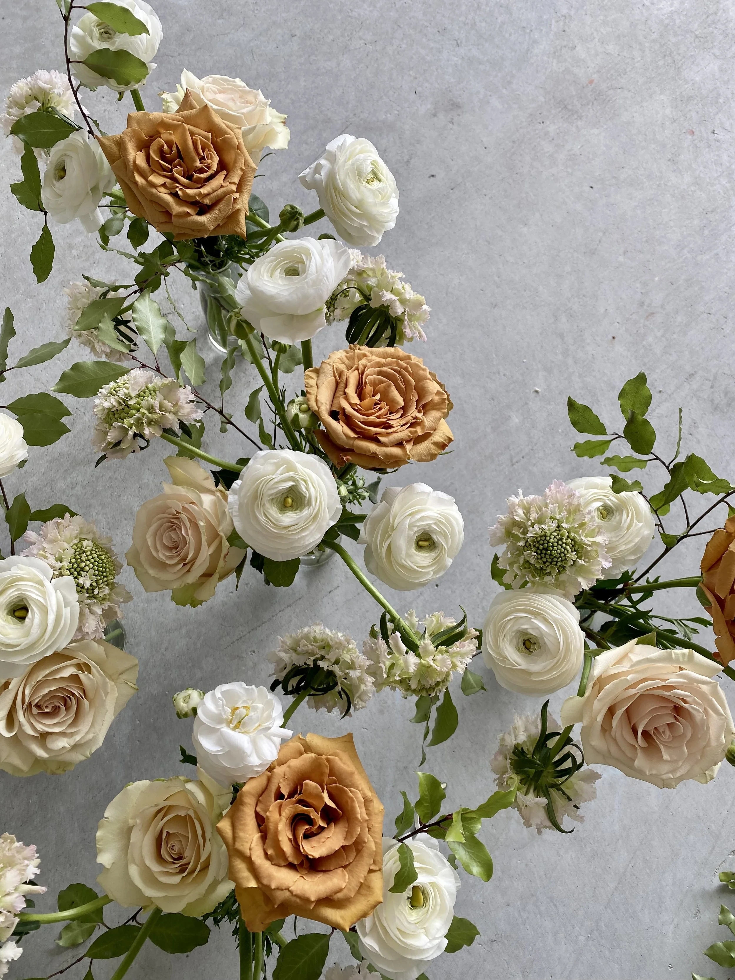 Various white, cream, and tan roses and flowers arranged on a gray surface.