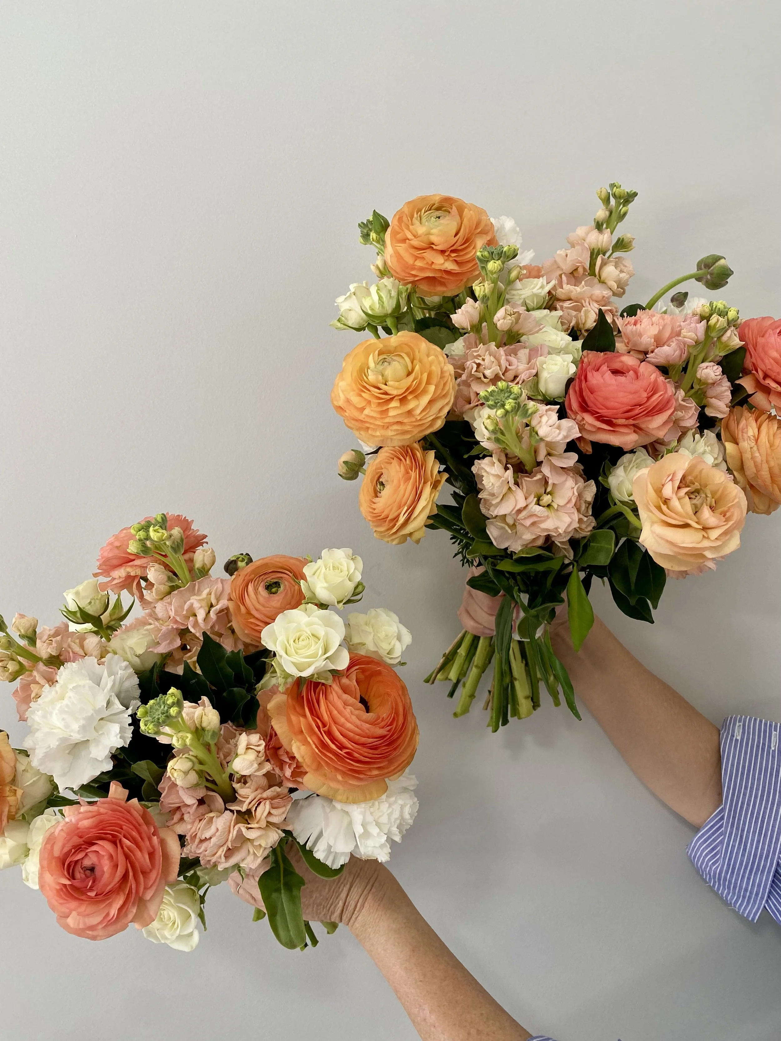 Two bouquets of mixed pink, white, and orange flowers being held against a plain white background.