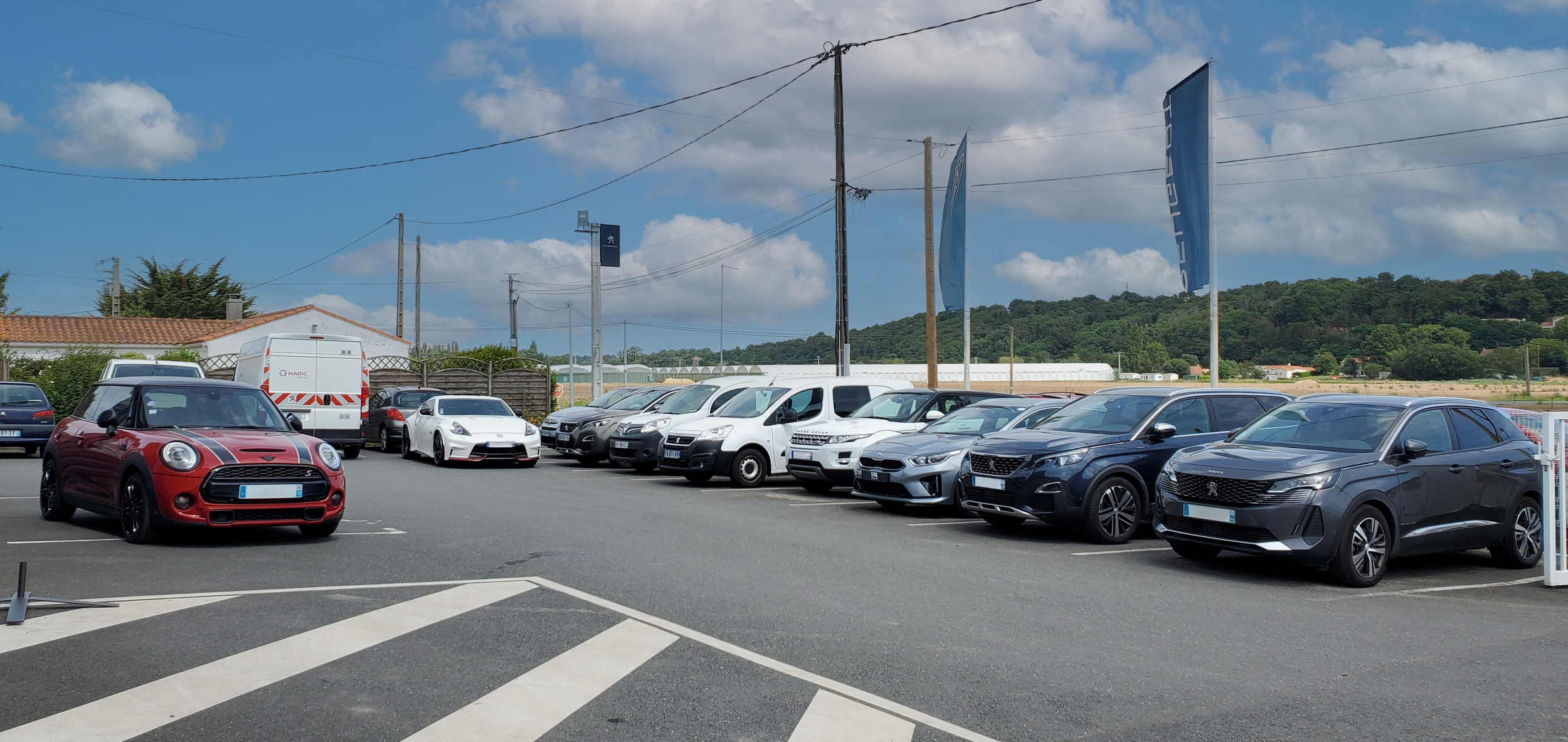 Voitures stationnées, avec un ciel partiellement nuageux et un paysage rural en arrière-plan.
