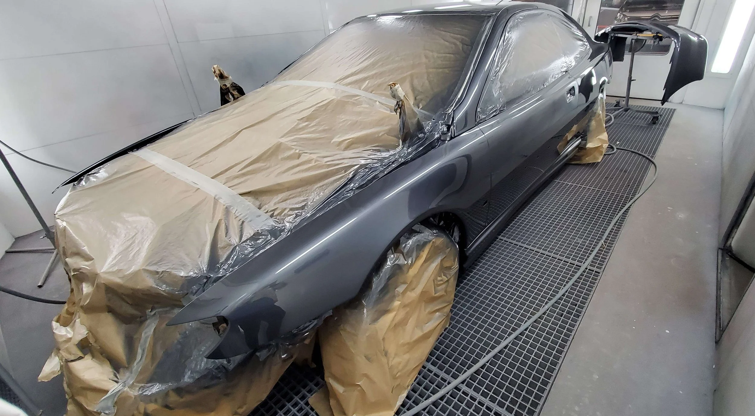Voiture en cours de peinture dans un atelier, recouverte de plastique et de papier de masquage, sur une grille de ponçage.