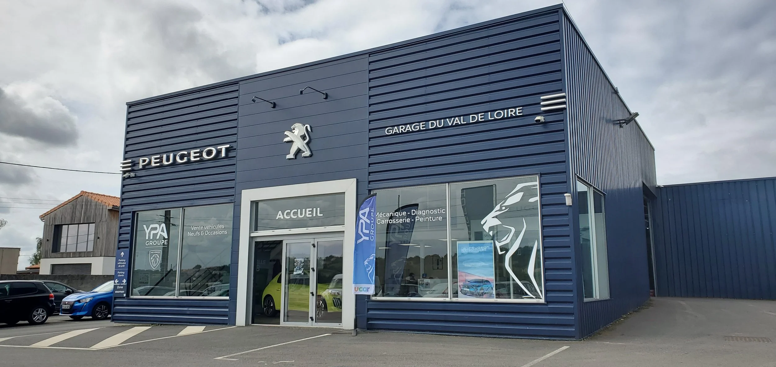 Concessionnaire Peugeot avec façade bleue, un logo de lion et une vitrine avec voitures exposées.