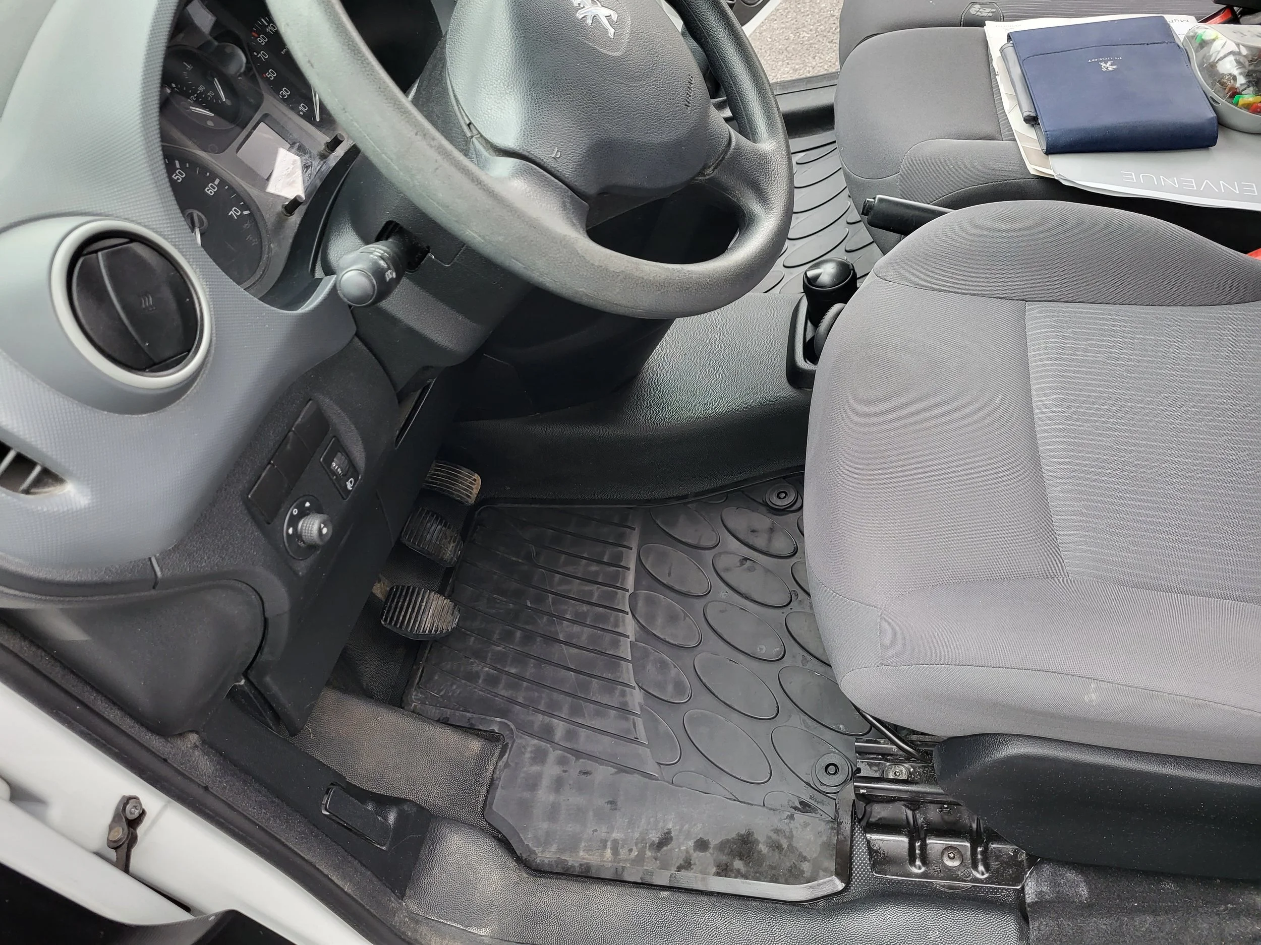 Intérieur d'une voiture avec tableau de bord, volant, pédales, siège conducteur et tapis de sol.