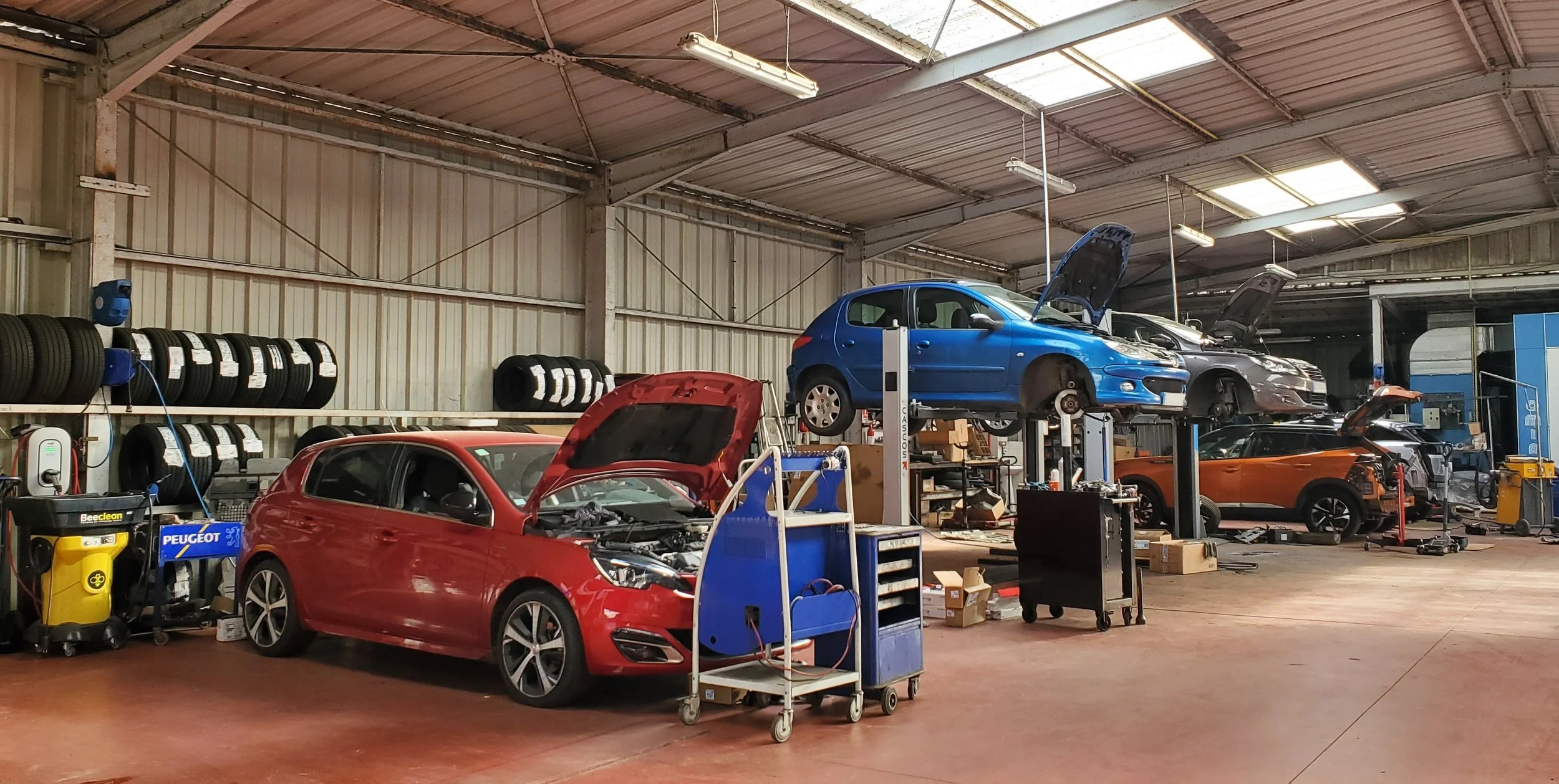 Un atelier de réparation automobile avec plusieurs voitures en cours de réparation, des pneus empilés, et des outils de travail.