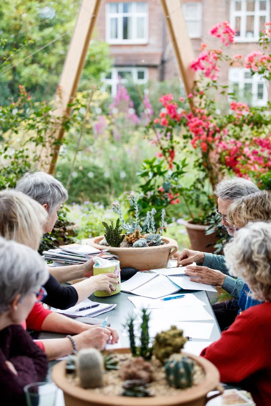 Mensen die een bijeenkomst of vergadering houden in een tuin, omgeven door bloemen en planten.