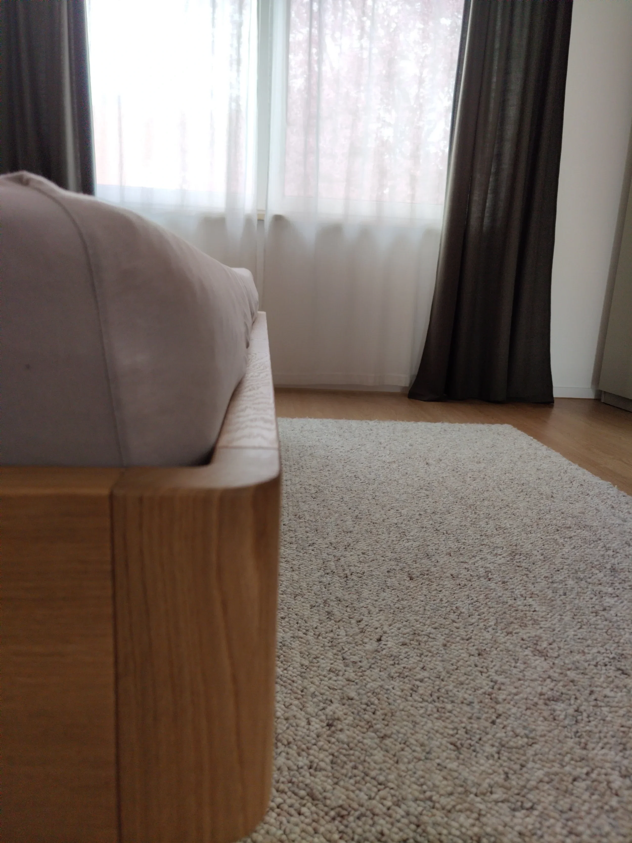 Ein Wohnzimmer mit Couch, Teppich, Fenster mit weißen und schwarzen Vorhängen, Holzfußboden.