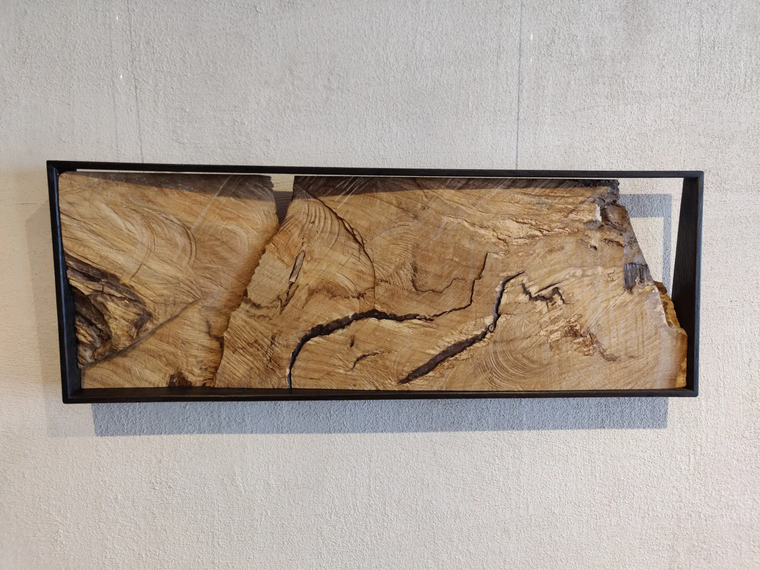 Holzstück in einem schwarzen rechteckigen Rahmen, an einer Wand befestigt.