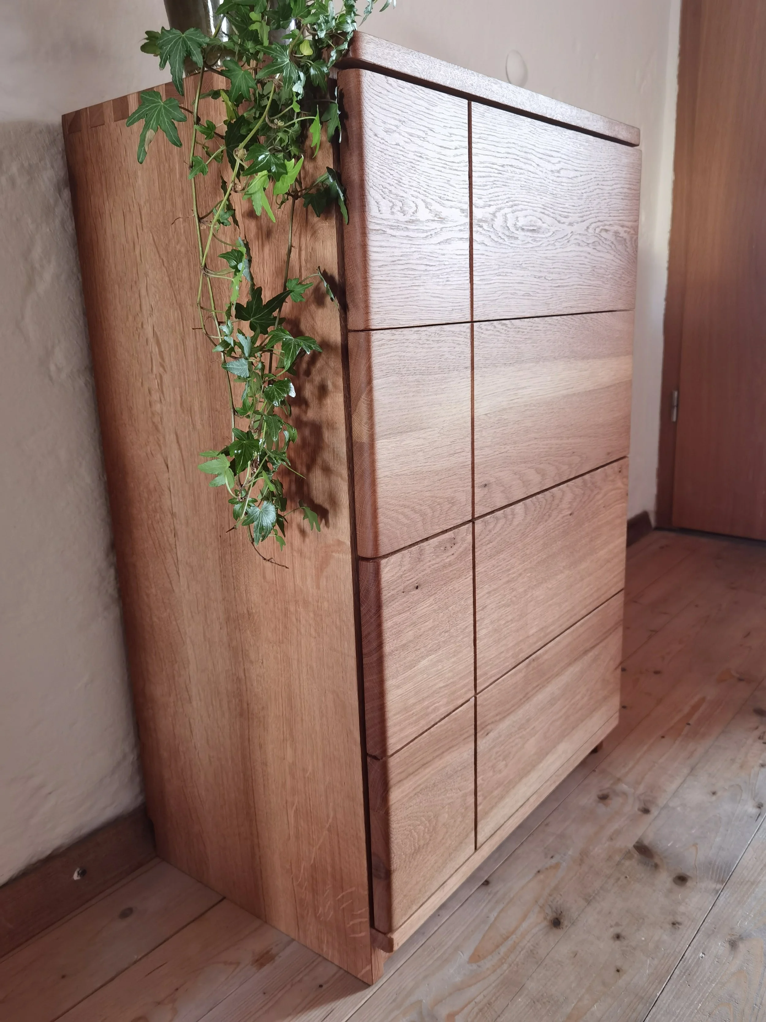Ein rustikaler Holztisch mit einer Topfpflanze auf der linken Seite, vor einer weißen Wand und einem Holztürrahmen.