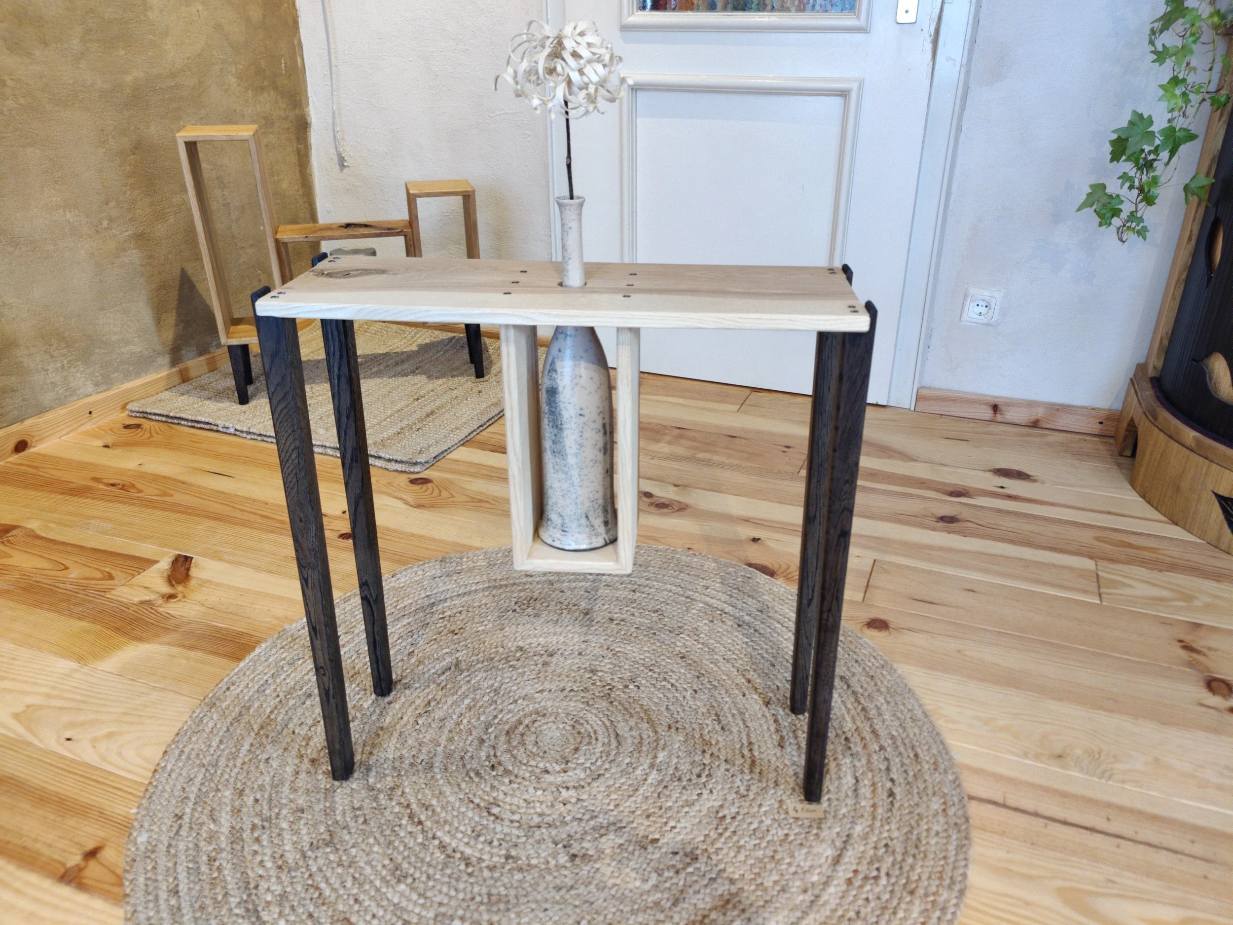 Ein stilvoller Tisch mit einer Vase in der Mitte, auf einem runden Teppich vor einer weißen Tür und Holzfußboden. Hinter dem Tisch befinden sich leere Holzstühle.