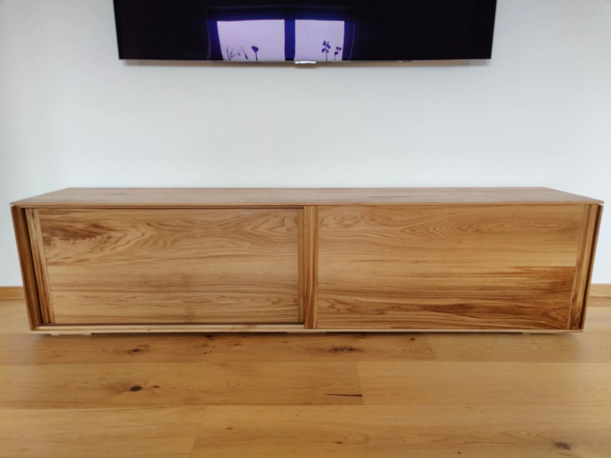 Ein modernischer Holztisch vor einer weißen Wand, an der eine Wandtafel mit Zeichnungen hängt.