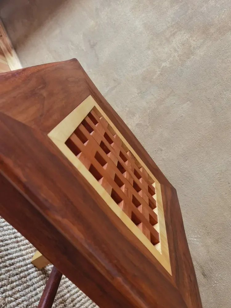 Holztisch mit einem Gittermuster in der Mitte, im Hintergrund ein Teppich und ein Betonboden.