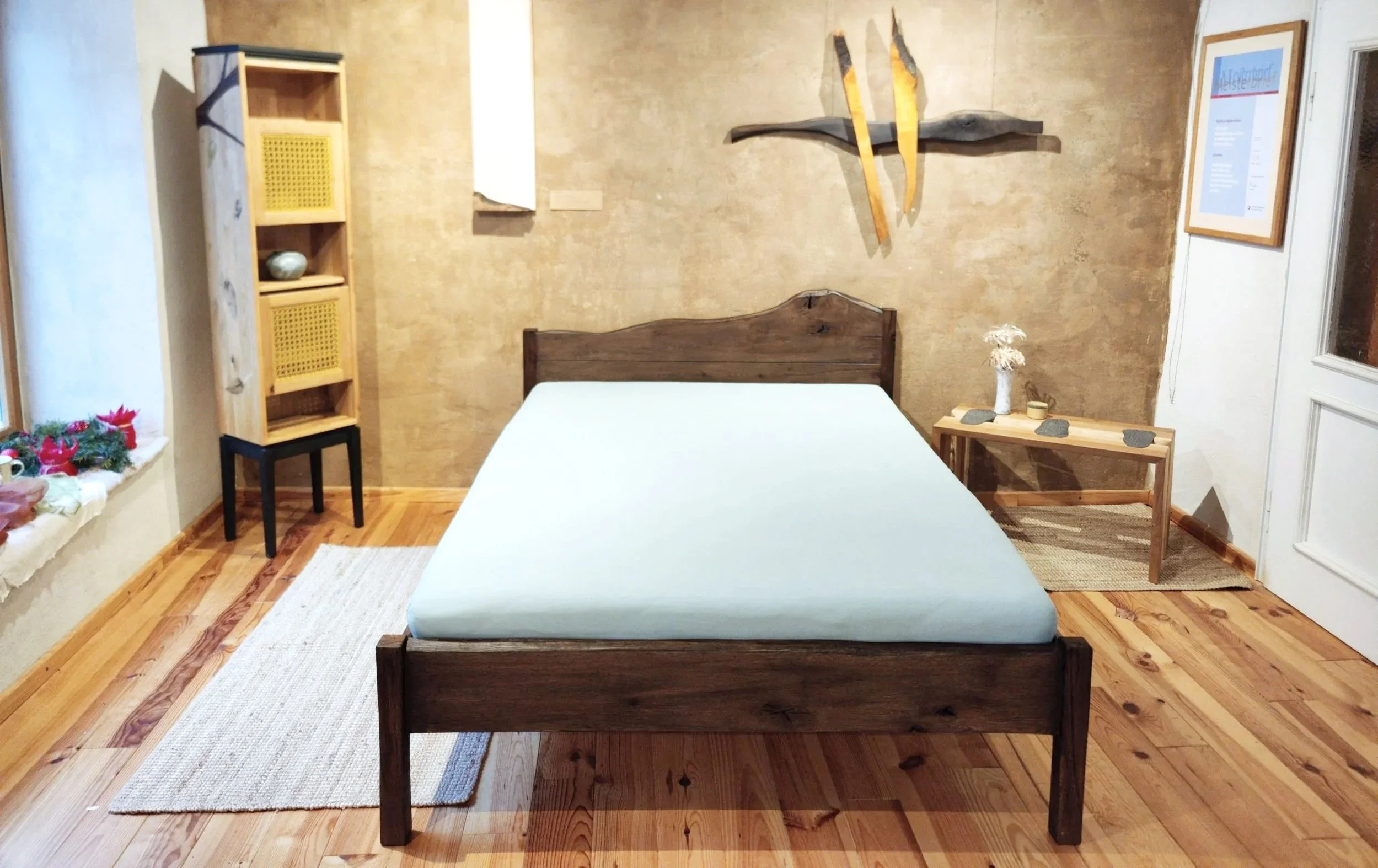 Ein Schlafzimmer mit einem Bett, das einen weißen Bezug hat, daneben ein kleiner Nachttisch mit Dekorationen, einen Holzregal, eine Fensterbank mit Weihnachtsdekoration, und Wandkunst an der Wand.