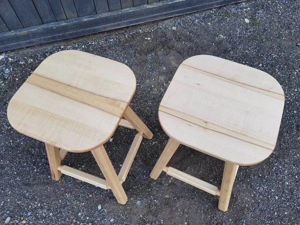 Zwei kleine hölzerne Hocker auf einer Steinfläche im Freien.