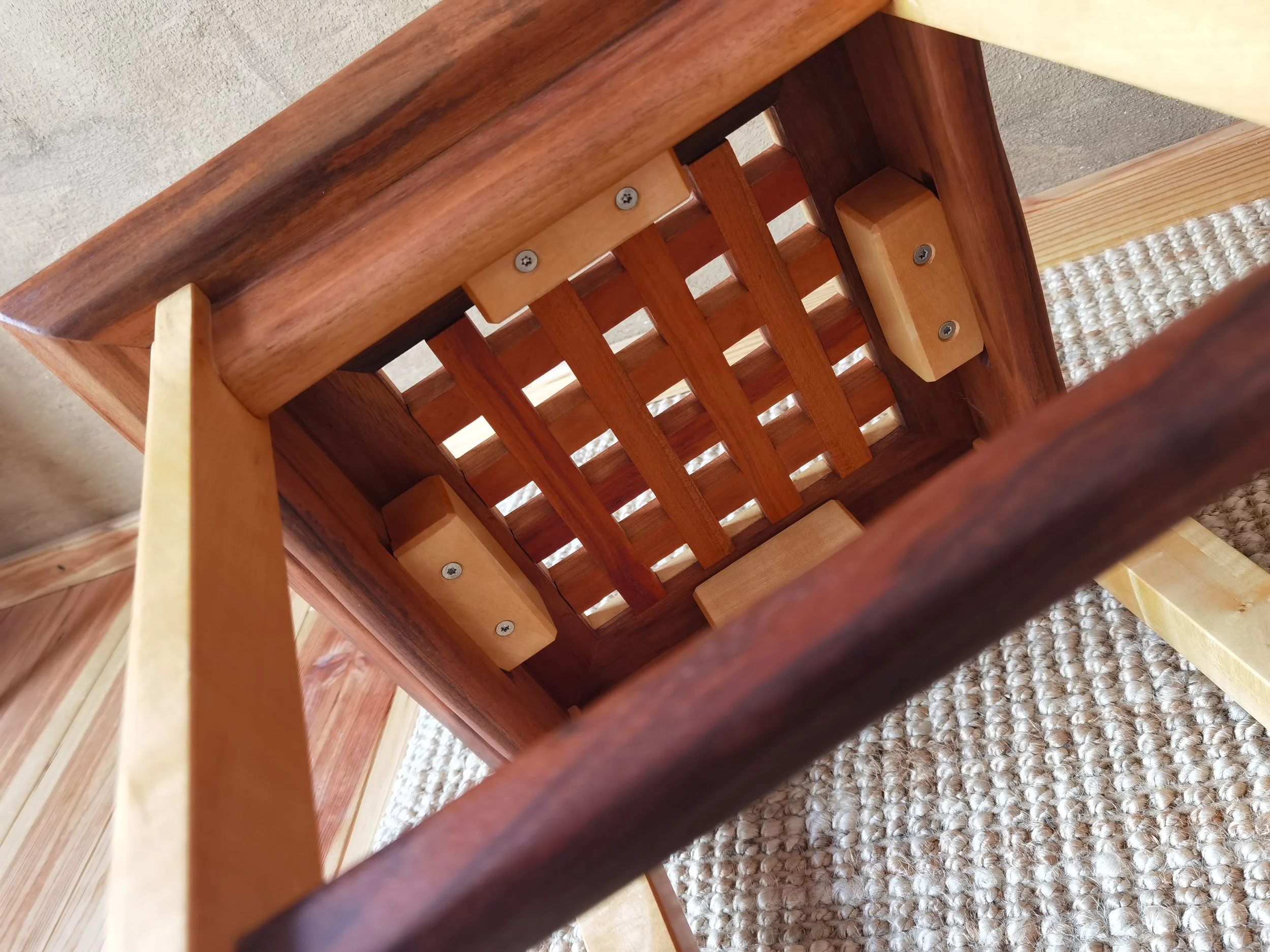 Innenansicht eines umgedrehten Stuhls aus Holz mit Holzlatten und Schrauben, auf einem Teppichboden.