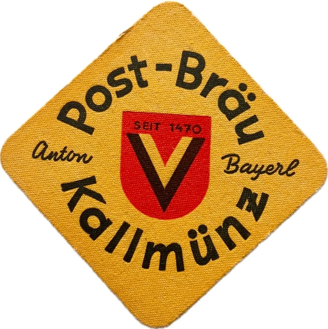 Ein gelbes Stoffabzeichen mit schwarzem Text, einem roten Wappen in der Mitte und schwarzen Kalligraphie-Schriftzügen. Der Text lautet 'Post-Bräu' oben, 'Anton Bayerl' links und 'Kollmünz' unten. Der rote Wappen enthält einen schwarzen Buchstaben 'V' und den Schriftzug 'Seit 1470'.
