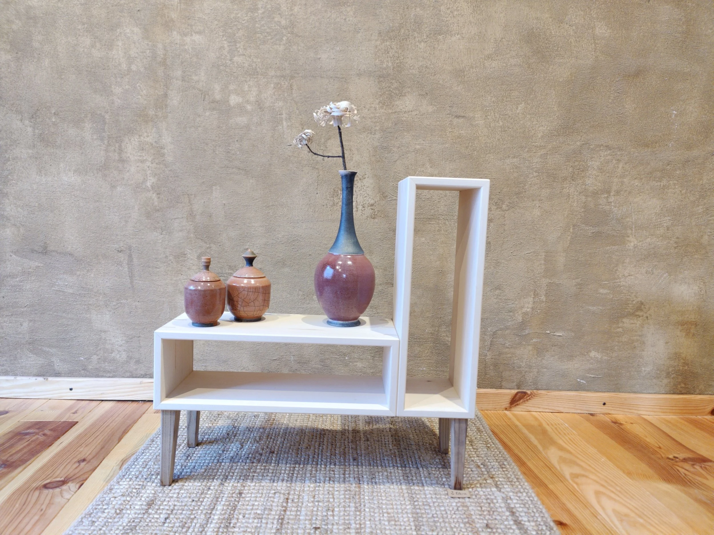 Drei Keramikvasen mit Blumen auf einem modernen weißen Beistelltisch, der vor einer rohen Betonwand steht.