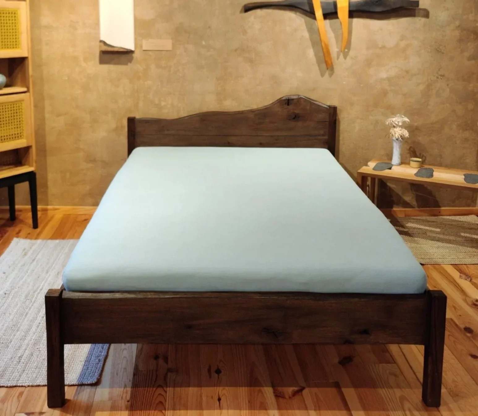 Ein Schlafzimmer mit einem Holzbett, einem Nachttisch mit Dekoration und einer Stehlampe an einer Natursteinwand.