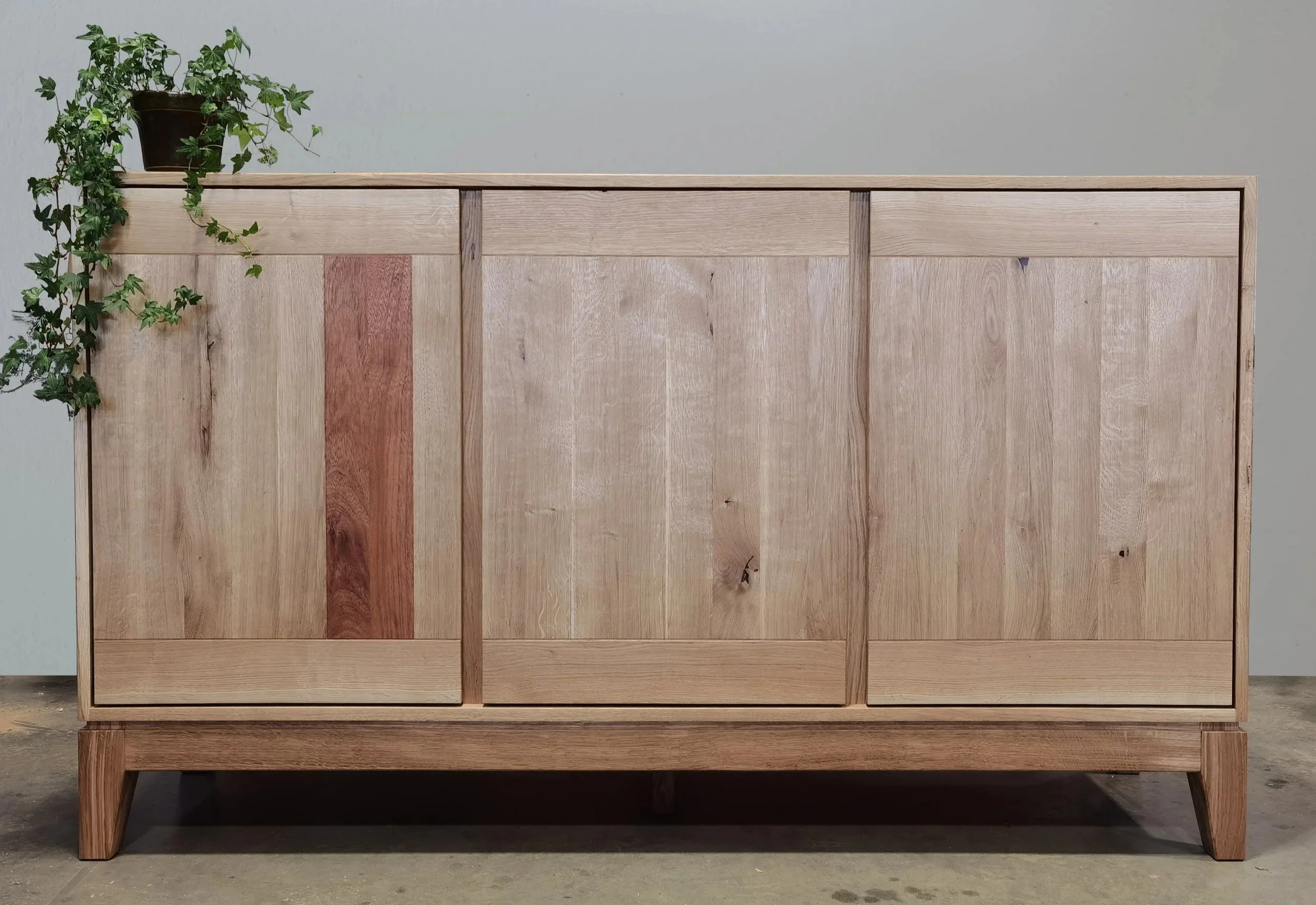 Holzsideboard mit drei Türen, auf dem ein Topfpflanze steht.