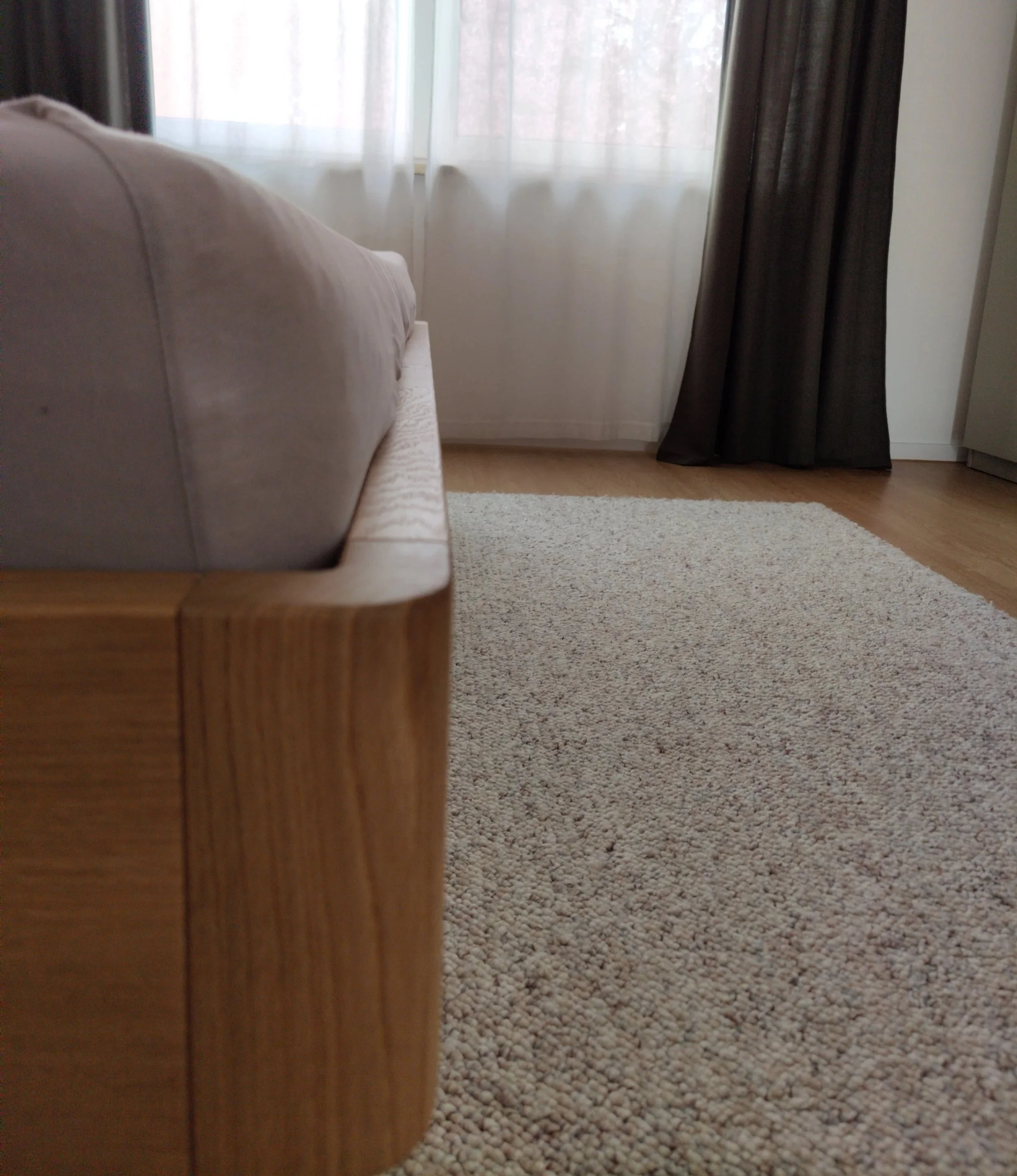 Ein gemütlicher Raum mit einem beige Couch, einem beige Teppich, weißen Vorhängen und schwarzen Vorhängen, Holzfußboden.