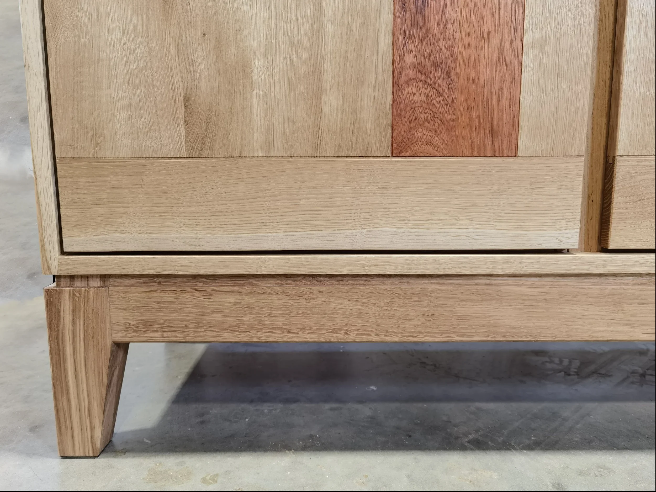 Nahaufnahme eines Teils eines Holzschranks mit vier Beinen auf einem Betonboden.