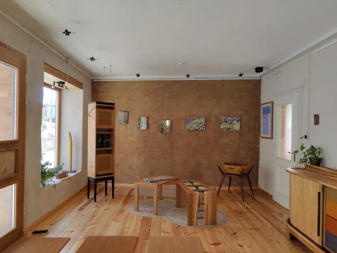 Ein gemütliches Wohnzimmer mit Holzmobiliar, Wandbildern und großen Fenstern mit Vorhängen.