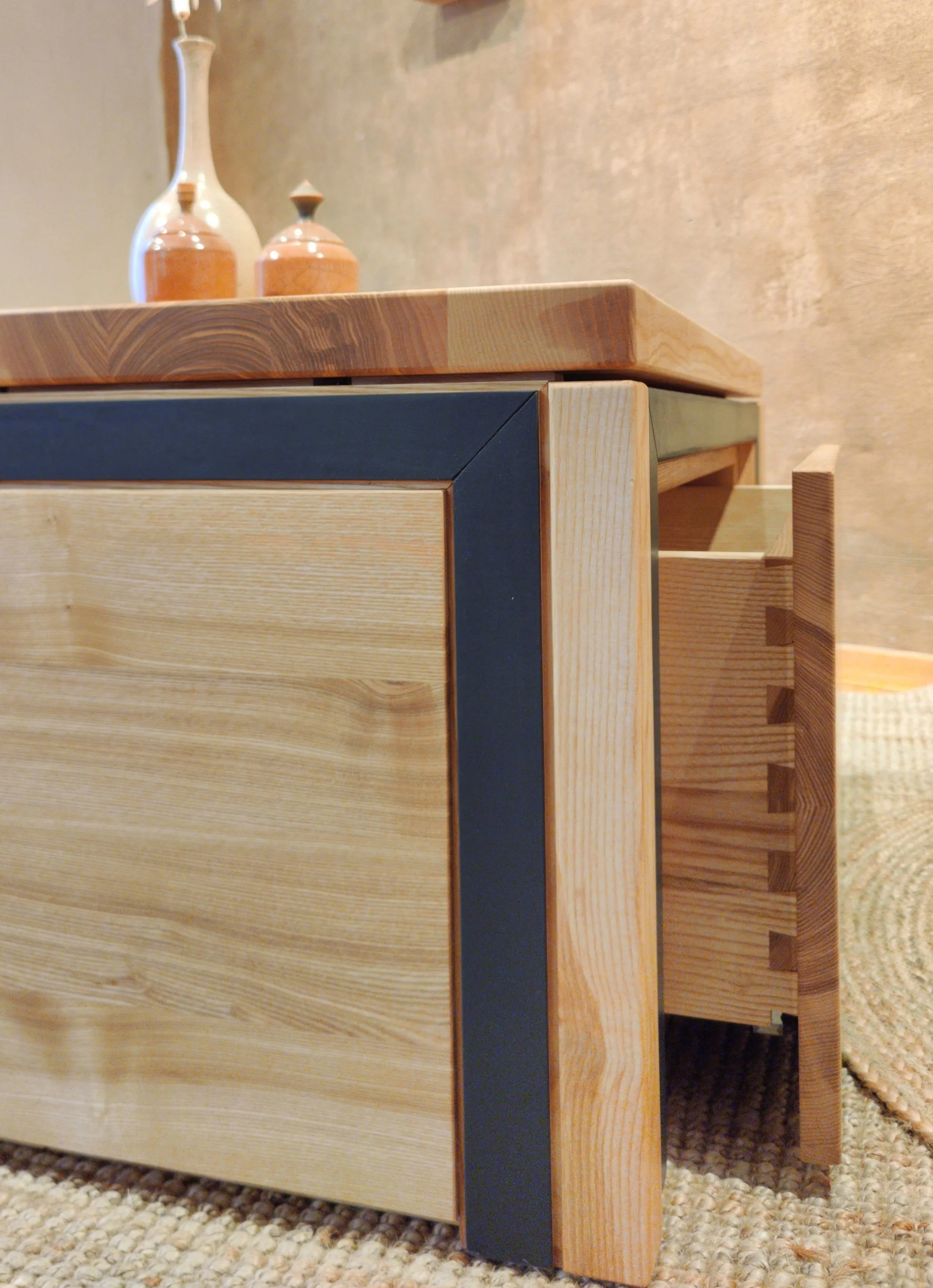 Nahaufnahme eines Möbelstücks aus Holz mit schwarzem Akzent, zusätzlich sind zwei Keramikvasen auf der Oberfläche zu sehen.