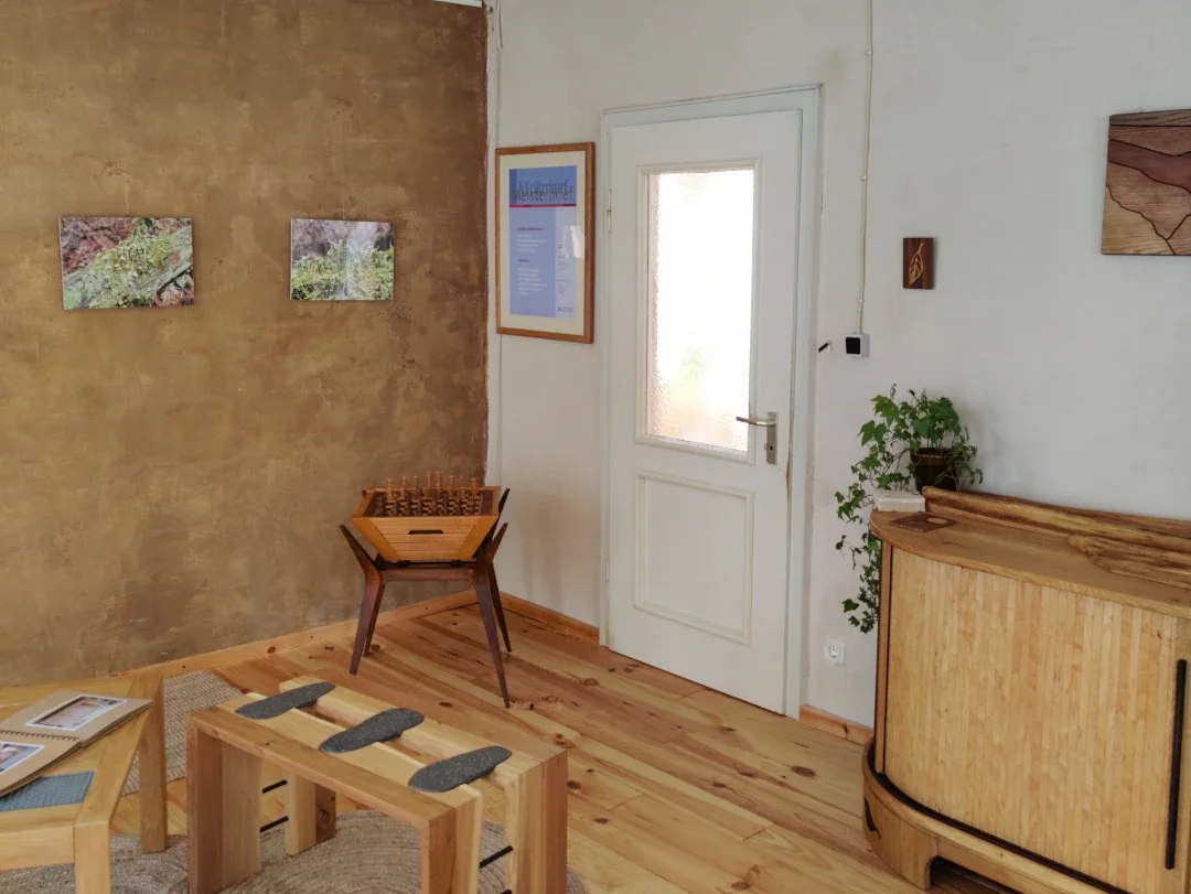 Innenraum eines Raums mit Holzmöbeln, Pflanzen und Kunstwerken an den Wänden.