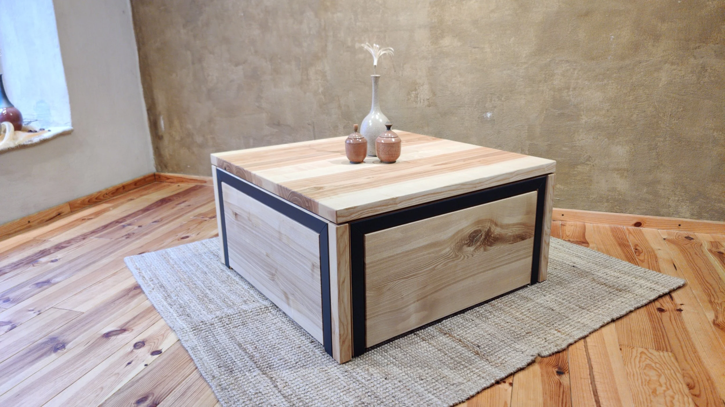 Holztisch mit Metallrahmen und Holzmaserung, steht auf einem Wollteppich in einem Raum mit Holzboden und einer braunen Wand.