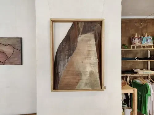 Ein Gemälde in einem Holzrahmen, das eine Holzwand oder einen Flur darstellt, hängt an einer weißen Wand in einem Raum.