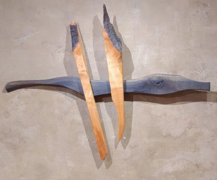 Holzskulptur: Zwei Holzstücke, die wie Flügel oder Vögel aussehen, sind an einer Wand befestigt.