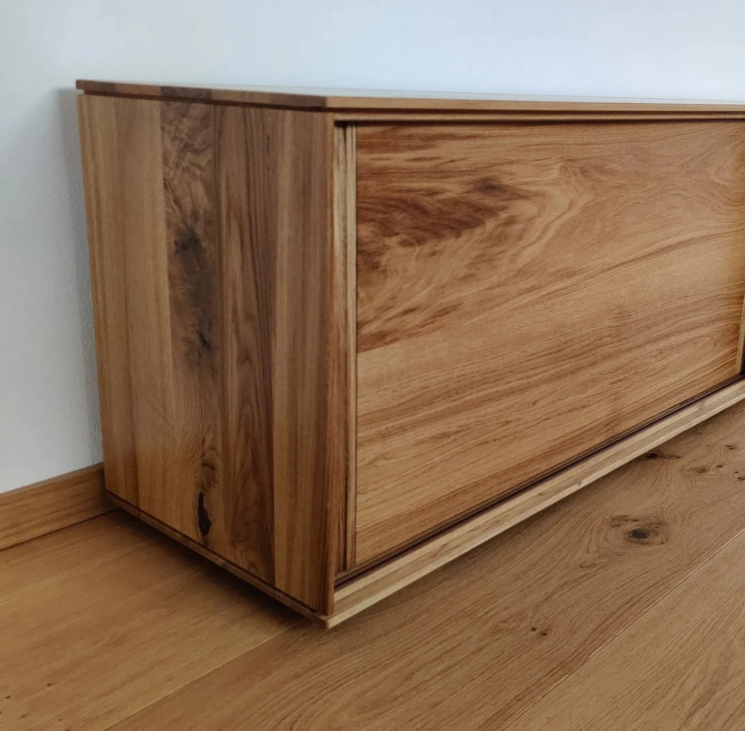 Ein Holz-Mock-up in hellem, naturfarbenen Holzmaserung, in einer Ecke neben einer weißen Wand und einem Holzboden.