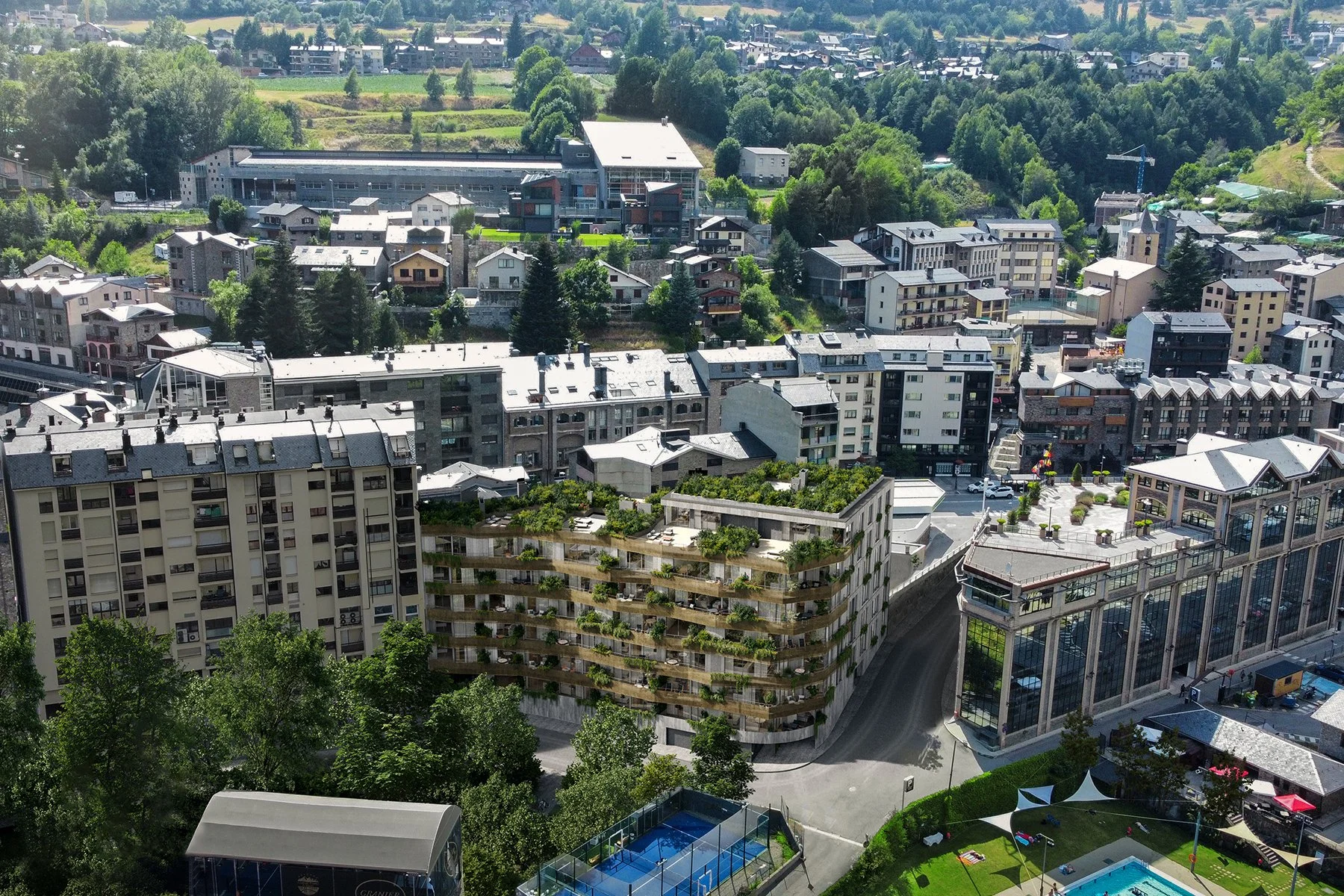 Vista aérea de un área urbana con edificios residenciales y comerciales rodeados de árboles y colinas verdes.