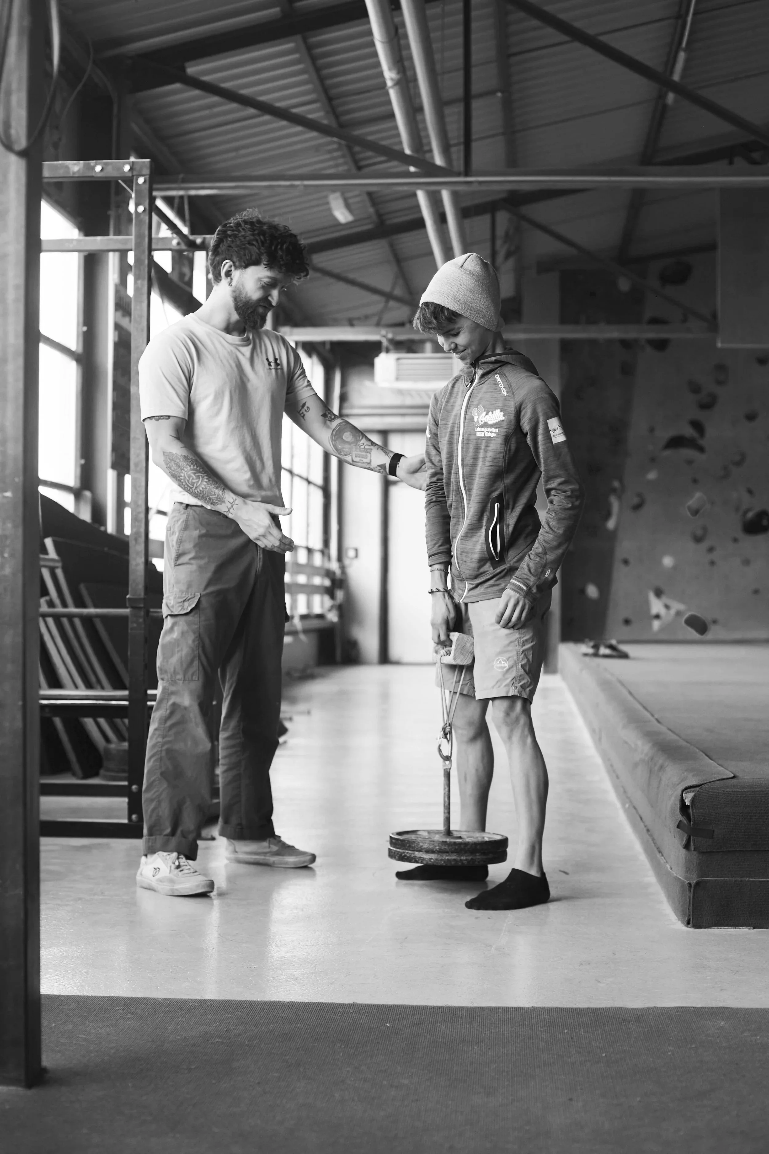 Ein Trainer erklärt einem jungen Kletterer im Fitnessstudio die Verwendung eines Gewichts.