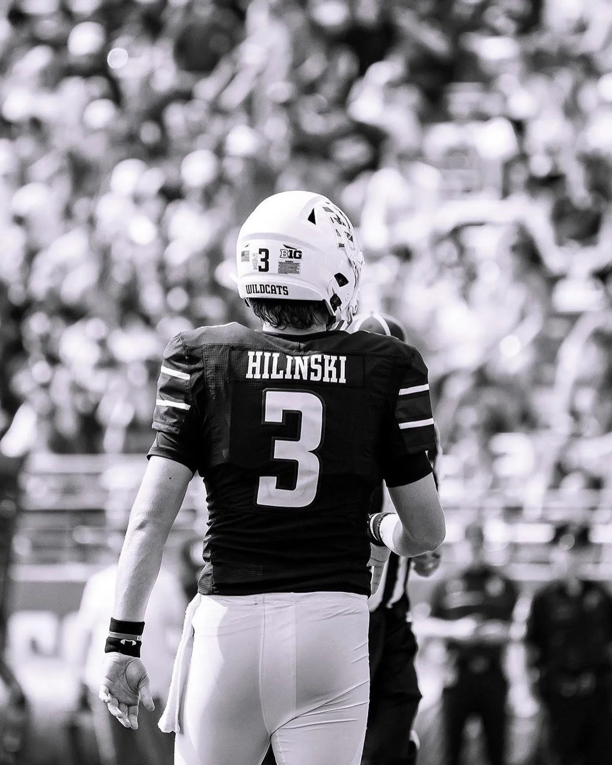 A football player wearing a jersey with the name 'HILINSKI' and the number 3, walking on the field with a helmet on. The background shows a crowd at a stadium.