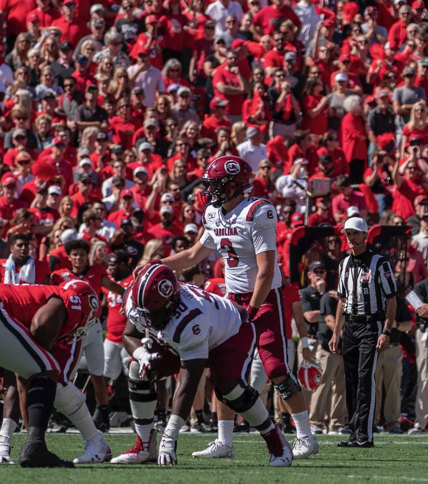 A football game with players in white and red uniforms on the field, with a crowd dressed mostly in red in the stands.