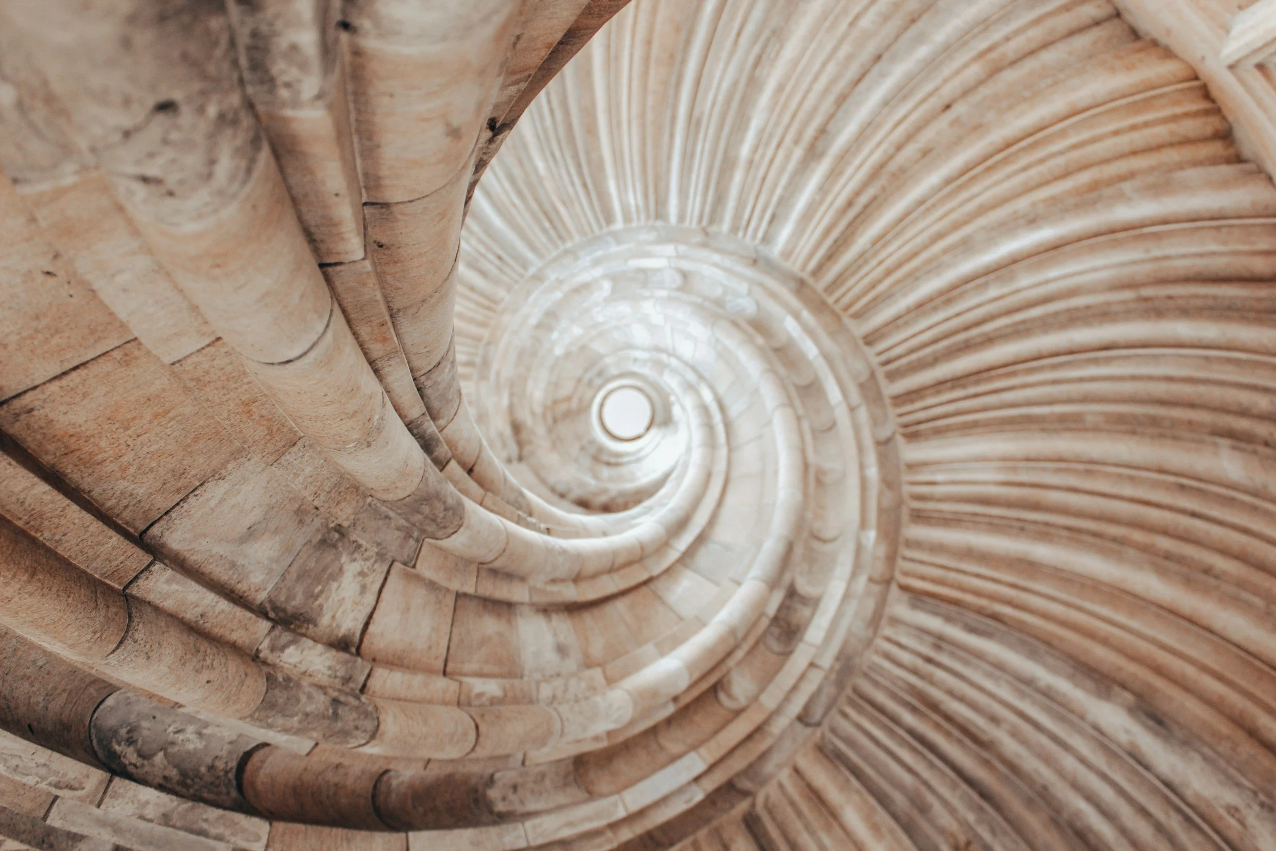 Looking up inside a spiral stone staircase, showing the circular pattern and texture of the bricks and stone.