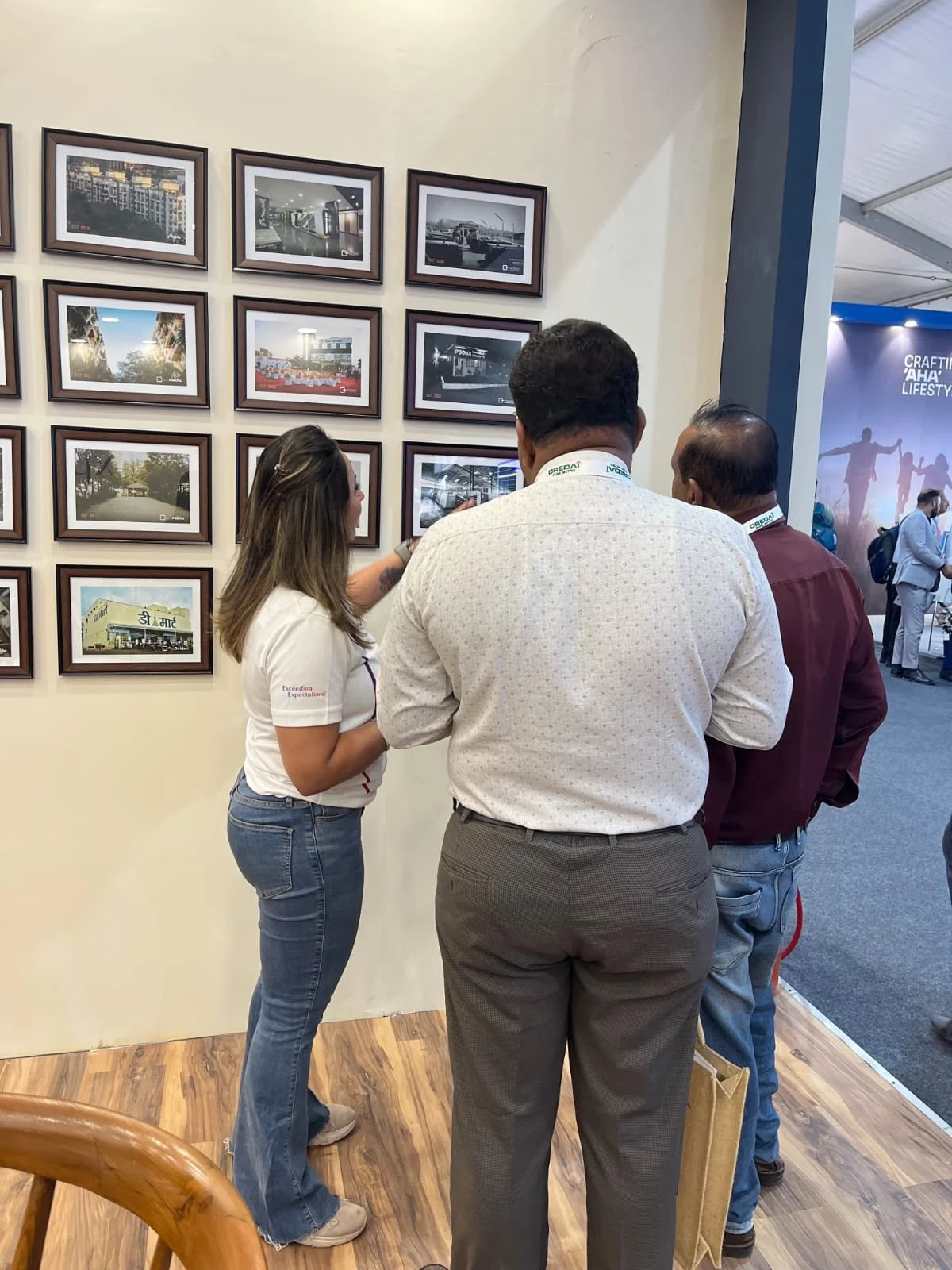 Group of three people looking at framed photographs on a wall in an exhibition or gallery.