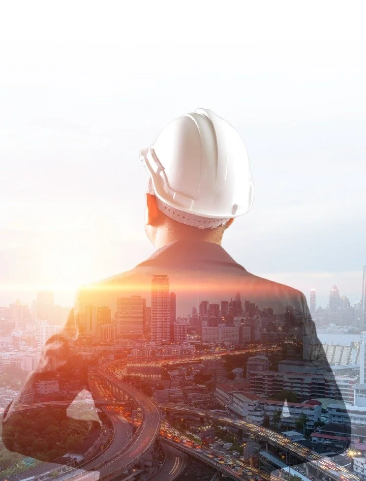 A double exposure photograph of a construction worker wearing a white hard hat, superimposed over a cityscape at sunset with tall buildings and highways.
