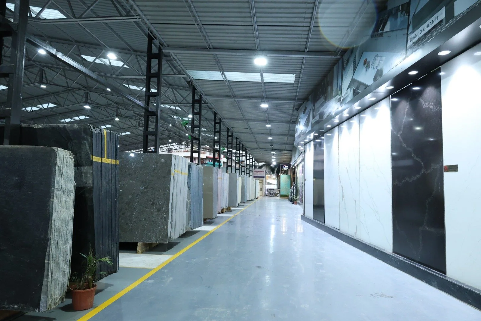 Indoor showroom with large slabs of marble and granite on display, illuminated by ceiling lights, with a polished concrete floor and a metal roof structure. Ceratec Marble.